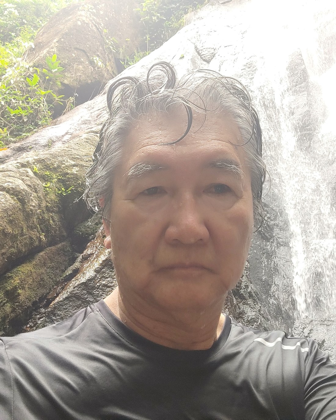 Oscar Yonesake em uma trilha, parado diante de uma cachoeira